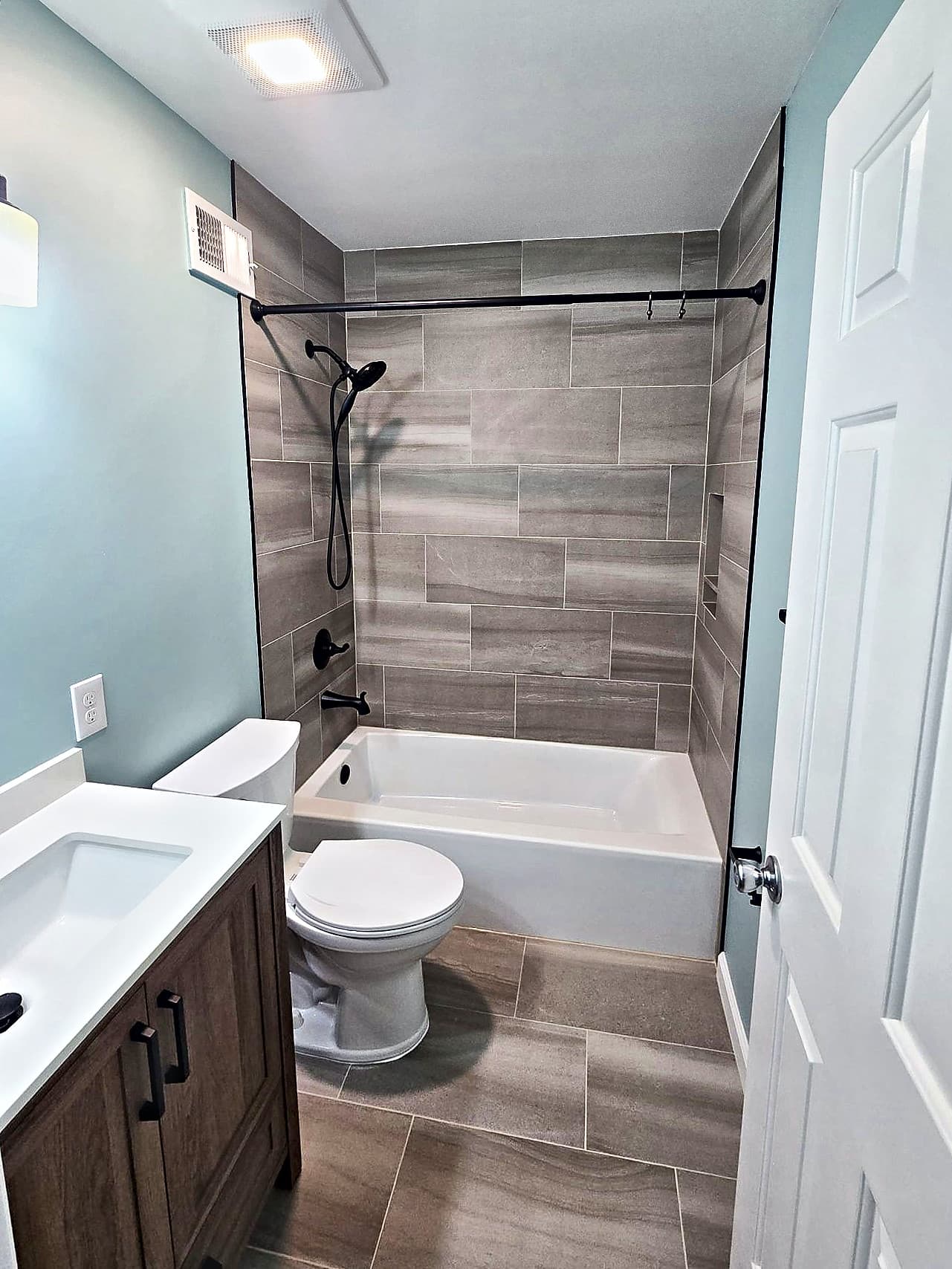 Remodeled hall bathroom in Ambler with a wood vanity, low-sided tub and gray tile surround