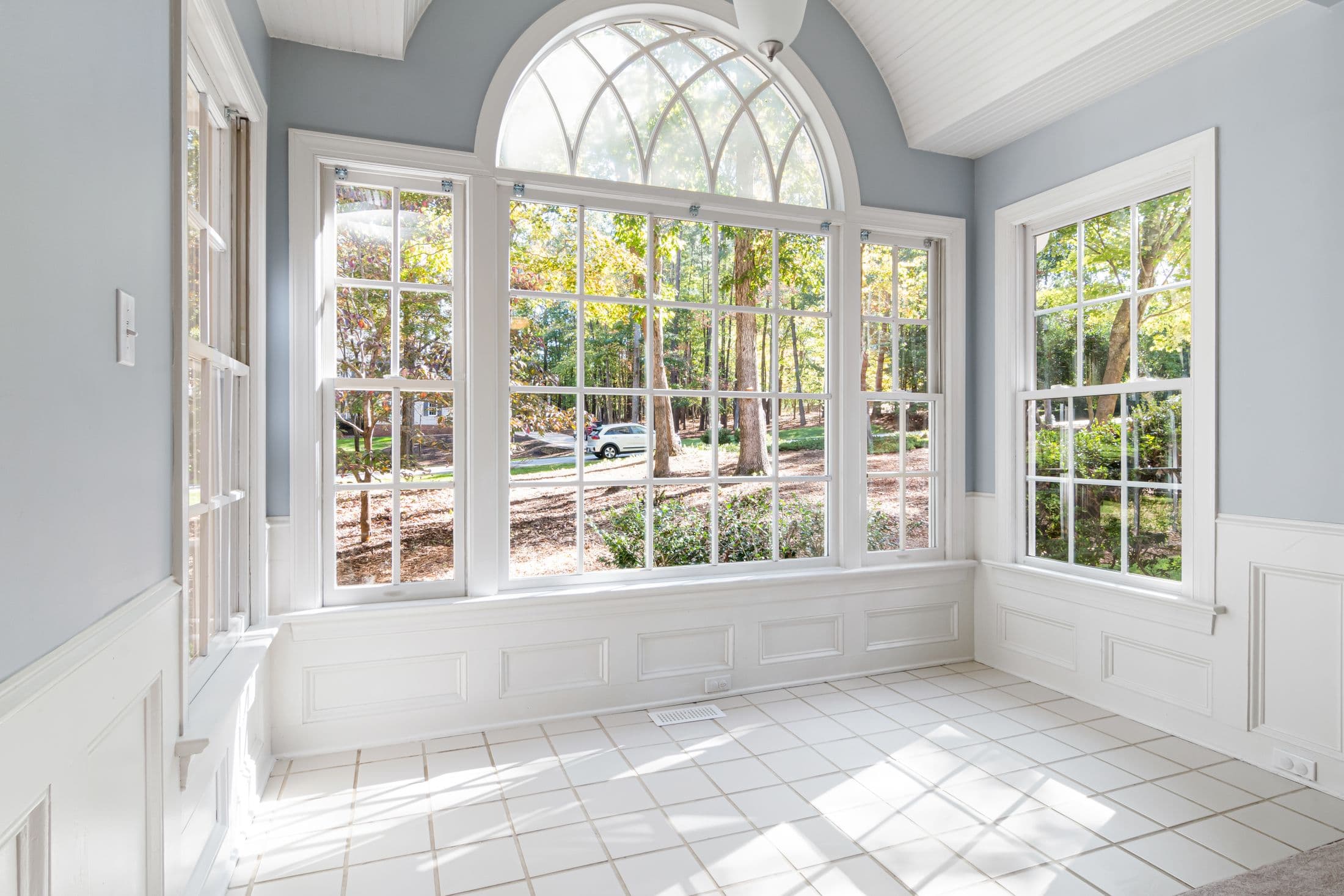Bright sunroom with an arched window, white trim and tiled floor