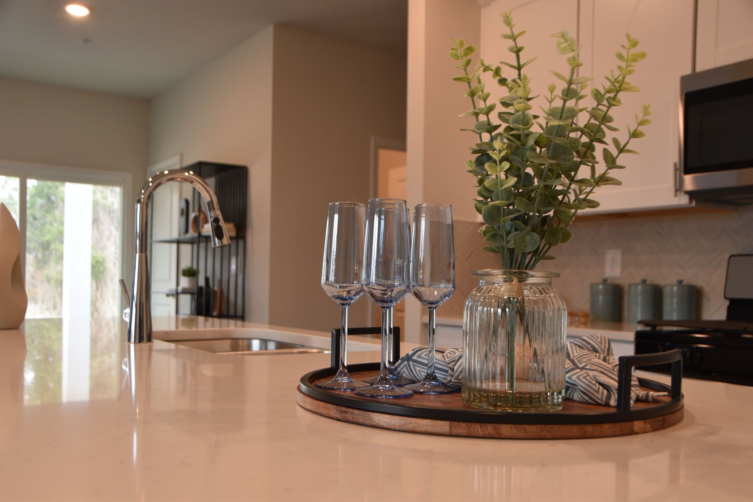 Kitchen island with a quartz countertop, glassware, and greenery in a bright remodeled kitchen